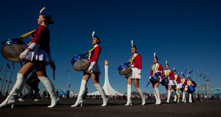Cheerleaders walk to a venue past the burning Olympic cauldron during the 2014 Winter Olympics in Sochi, Russia, Feb. 13, 2014. 