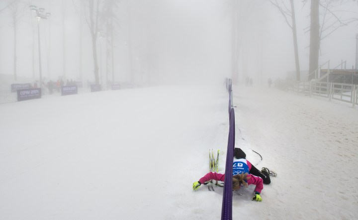 Biathlete Laure Soulie of Andorra crawls under a barricade onto the course to practice in heavy fog during a delay prior to the Men's Biathlon 15km competition at Laura Biathlon Center.