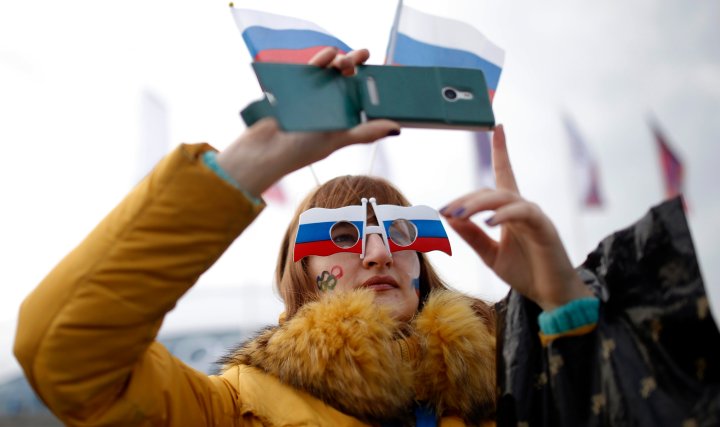 A woman sports the Russian national flag with her eyewear and takes photographs with a smart phone at Olympic Park during the 2014 Sochi Winter Olympics, Feb. 11, 2014.  